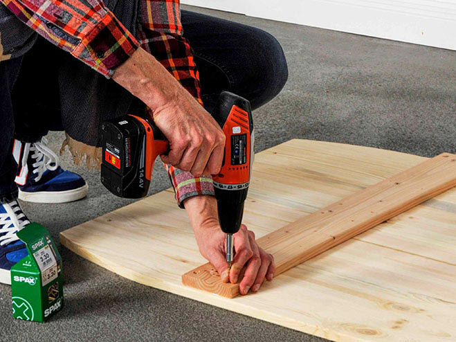 Mit einem Akkubohrer wird eine Querstrebe auf die übrigen Holzbretter montiert