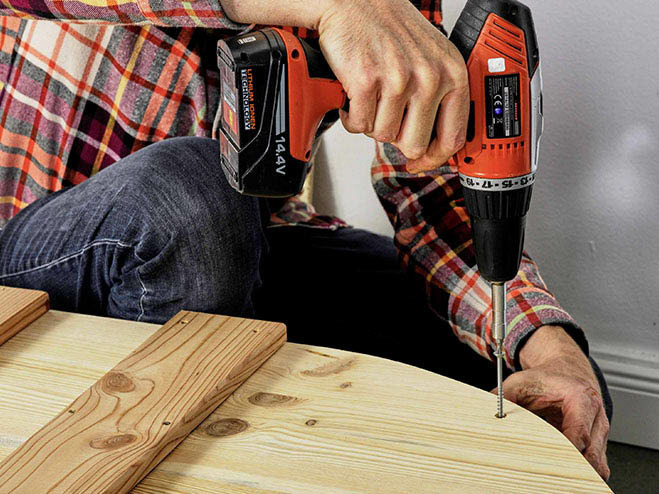 Mit einem Akkubohrer wird in ein Holzbrett ein Loch gebohrt