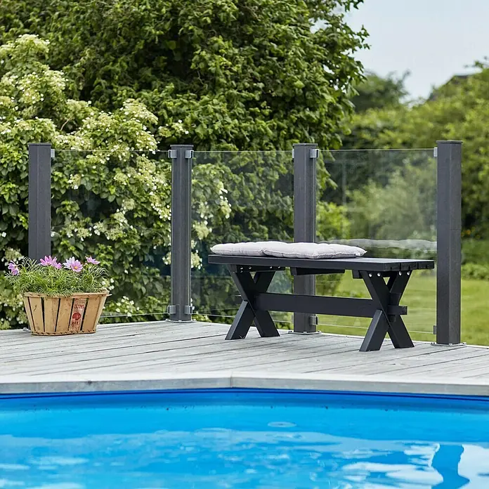 Plus Sichtschutzelement Futura Klar - 90 x 91 cm, Glas, Transparent - Eine schwarze Gartenbank mit einem grauen Kissen steht auf einer Holzterrasse neben einem Pool und einem Geländer aus Glas.