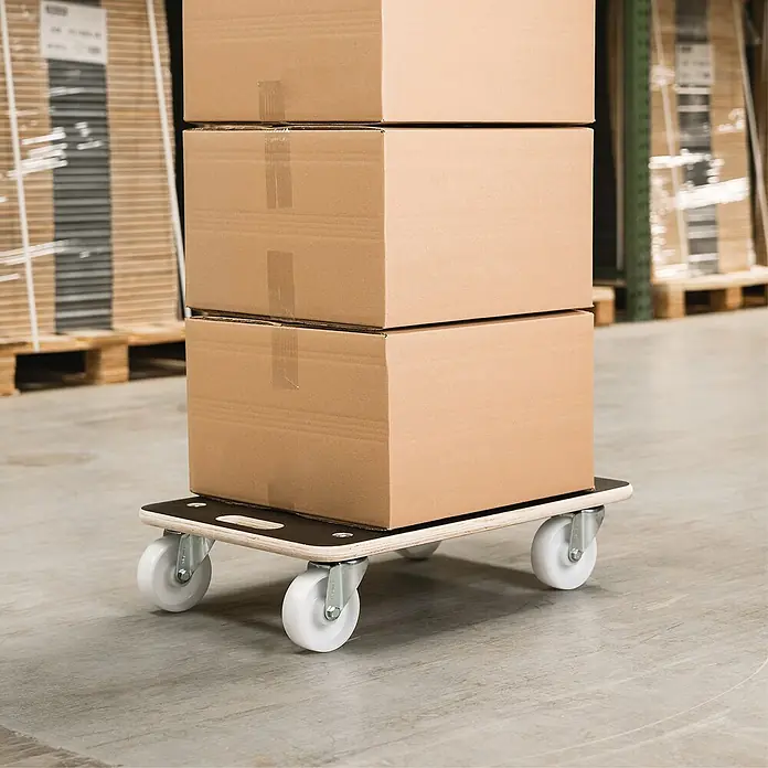 Wagner System Base con ruedas MM 1609 - L x An x Al: 57,5 x 29 x 11 cm, Capacidad de carga: 250 kg, Madera - Un tablero rodante con tres cajas de cartón apiladas en un almacén. El tablero rodante facilita el transporte de cargas pesadas.