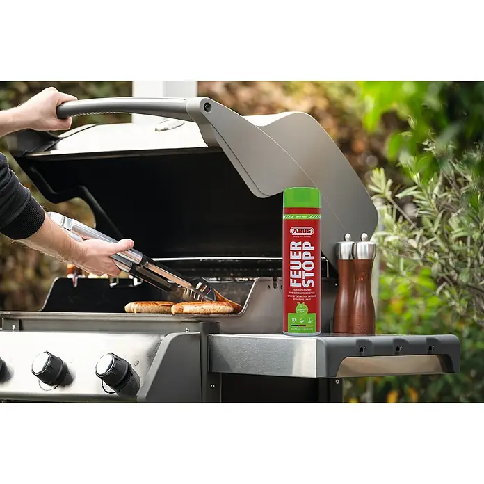 Abus Feuerlöschspray AFS625 - Geeignet für: Elektrische Anlagen bis 1.000 V (min. Abstand 1 m), 625 ml - Abus Feuerstopp auf einem Grilltisch neben einem Grill, auf dem Würstchen zubereitet werden.