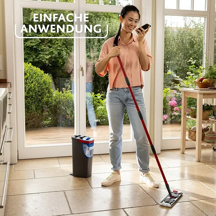 Vileda Reinigungssystem & Eimer H2PRO Flat Mop System - 1 x Flachwischer, 1 x Eimer mit Zweitanksystem, 1 x Wischbezug - Frau telefoniert und wischt mit dem Vileda Bodenwischer den Boden. Im Hintergrund steht der dazugehörige Eimer mit Auswringer.