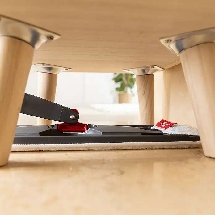 Vileda Reinigungssystem & Eimer H2PRO Flat Mop System - 1 x Flachwischer, 1 x Eimer mit Zweitanksystem, 1 x Wischbezug - Detailaufnahme eines Vileda Bodenwischers unter einem Tisch, der die Reinigung unter Möbeln demonstriert.