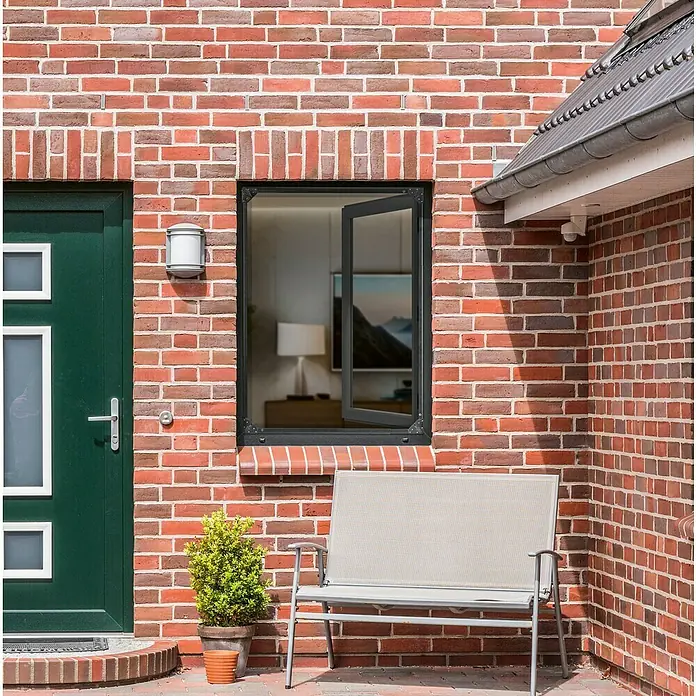 Easy Maxx Insektenschutzfenster - B x H: 115 x 135 cm, Montage Insektengitter: Klemmen, Farbe Rahmen: Anthrazit - Außenansicht eines Hauses mit einem modernen Fenster mit schwarzem Rahmen, einer grünen Tür und einer Gartenbank vor einer Ziegelmauer.