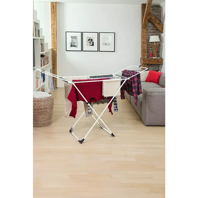 Vileda Flügel-Wäscheständer Universal - Länge Wäscheleine: 18 m, Weiß/Schwarz - Ein Wäscheständer mit darauf hängender Wäsche im Wohnzimmer, vor einem Sofa und unter Bildern.