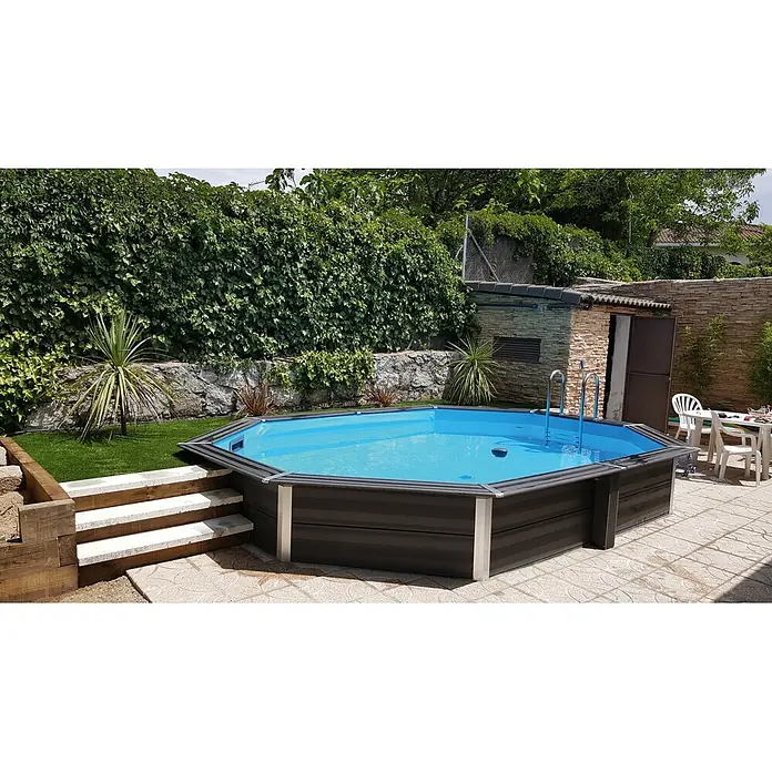 Gre Avantgarde WPC-Pool - L x B x H: 664 x 386 x 124 cm, 21.500 l, Dunkelgrau - Ein achteckiger Aufstellpool im Garten mit blauen Wasser und grauer Verkleidung, umgeben von Grünpflanzen und einem gepflasterten Bereich.