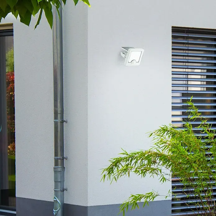 Brilliant Solar-Außenwandleuchte Luton - 4 W, L x B x H: 13 x 12 x 5,4 cm, Weiß, IP65, 540 lm - Weißer Outdoor-LED-Strahler an Hauswand, bietet Sicherheitsbeleuchtung neben einem Fenster.