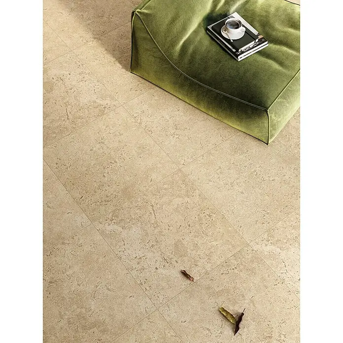 Corso Italia Terrassenfliese Pompei Aureo Crosscut - 60 x 60 cm, Beige, Matt - Ein grüner Sitzpouf mit einer Tasse und einem Buch darauf, auf einem gefliesten Boden, der eine entspannte Atmosphäre schafft.