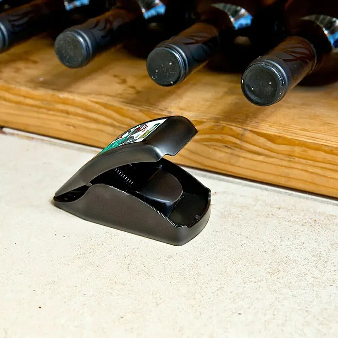 Windhager Mausefalle Snap - Spezialfalle, Kunststoff, 1 Stk. - Nahaufnahme einer schwarzen Mausefalle vor einem Weinregal, die Falle ist gespannt und bereit.