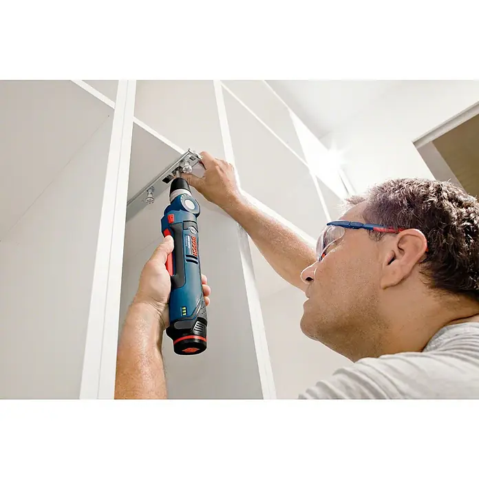 Bosch Professional Akku-Winkelbohrschrauber GWB 12V-10 L-Boxx - 12 V, Ohne Akku - Ein Mann befestigt mit einem Bosch Akku-Winkelschrauber eine Metallschiene an einer weißen Wand. Schutzbrille wird getragen.