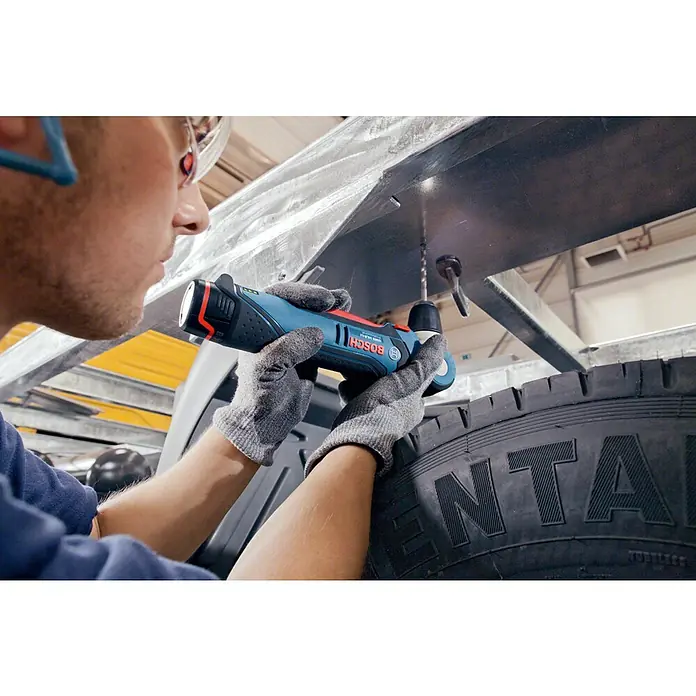 Bosch Professional Akku-Winkelbohrschrauber GWB 12V-10 L-Boxx - 12 V, Ohne Akku - Ein Handwerker bohrt mit einem Bosch Akku-Bohrschrauber ein Loch in ein Metallstück. Im Vordergrund ist ein Reifen zu sehen.