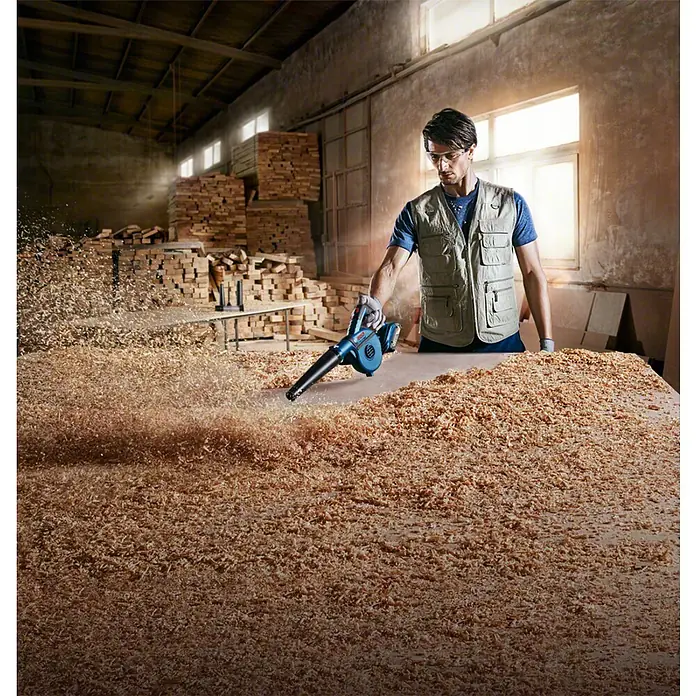 Bosch Professional AMPShare 18V Akku-Gebläse GBL 18V-120 - 18 V, Ohne Akku - Mann, der mit dem Bosch Laubbläser Holzhackschnitzel wegpustet. Ideal für die schnelle Reinigung von Werkstätten und Baustellen.