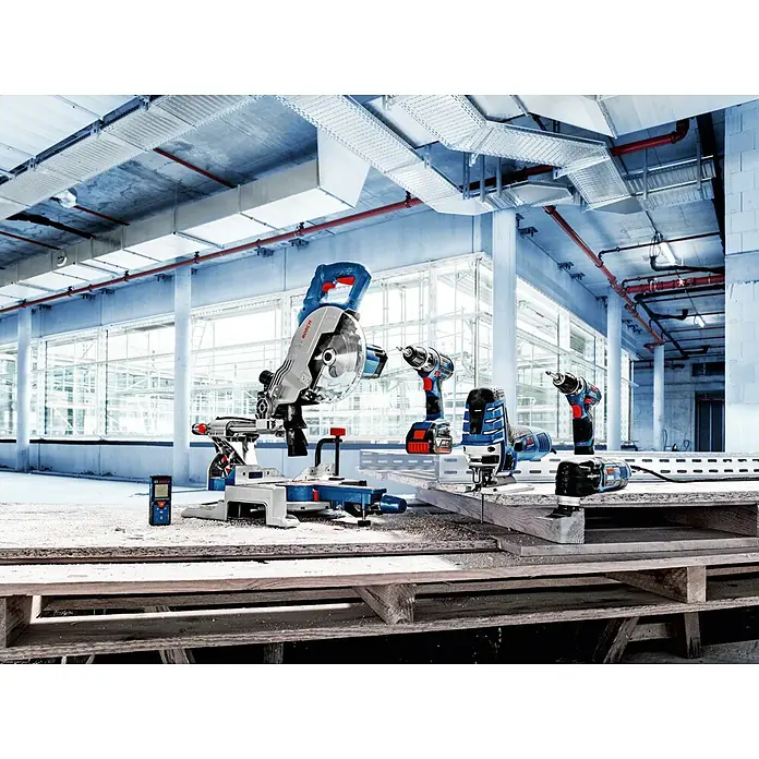 Bosch Professional Paneelsäge GCM 80 SJ - 1.400 W, Durchmesser Sägeblatt: 216 mm - Eine Auswahl an Bosch Elektrowerkzeugen, darunter Sägen, Bohrmaschinen und Schleifgeräte, präsentiert auf einer Werkbank in einer Lagerhalle.