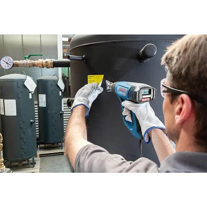 Bosch Professional Heißluftgebläse GHG 23-66 - 2.300 W, 50 °C - 650 °C - Ein Mann mit Schutzbrille verwendet eine Bosch Heißluftpistole, um ein Etikett an einem großen, zylindrischen Druckbehälter zu befestigen.