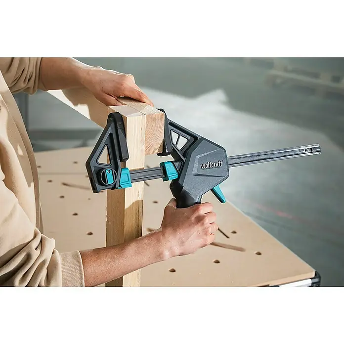 Wolfcraft Einhandzwinge Pro Max - Spannweite: 300 mm, Ausladung: 110 mm - Eine Wolfcraft Einhandzwinge wird benutzt, um zwei Holzstücke auf einer Werkbank zusammenzupressen.
