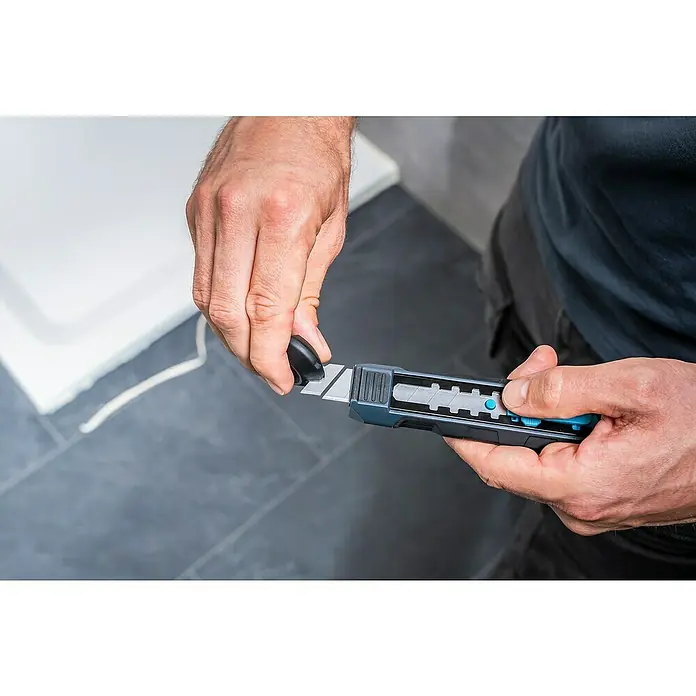Wolfcraft Schabermesser Dual - Typ Griff: 2K - Eine Person bricht mit einem dunkelgrauen Cuttermesser und blauem Akzent ein Klingenstück ab. Ideal für präzise Schneidearbeiten.