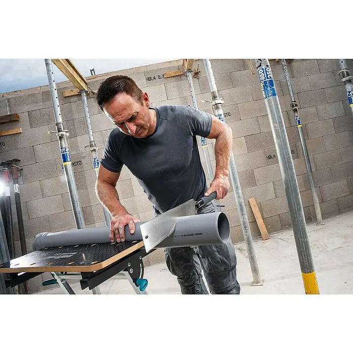 Wolfcraft Japansäge - Blattlänge: 330 mm - Ein Mann sägt ein graues Plastikrohr auf einer Werkbank. Im Hintergrund sind Stützen und eine Ziegelwand zu sehen.