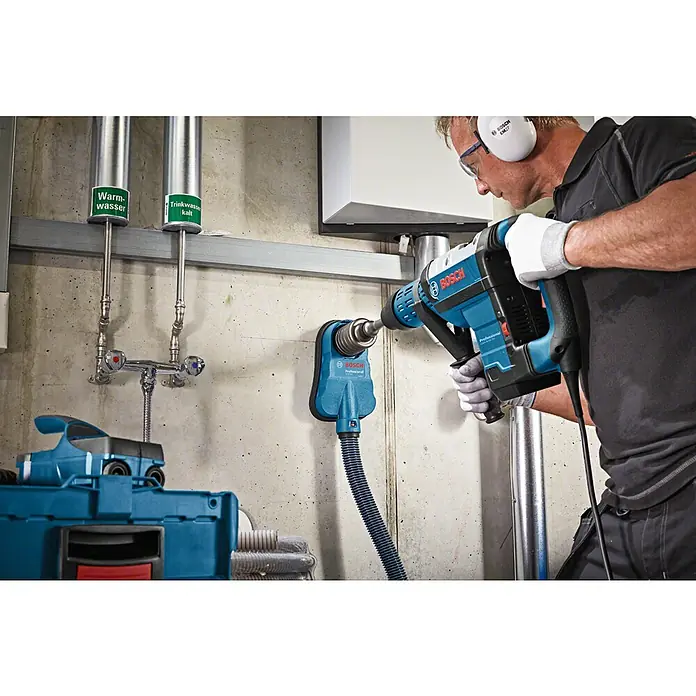 Bosch Professional Absaugvorrichtung GDE 68 -  - Ein Handwerker bohrt mit einem Bosch Bohrhammer in eine Wand, Staubabsaugung ist angeschlossen, um sauber zu arbeiten.