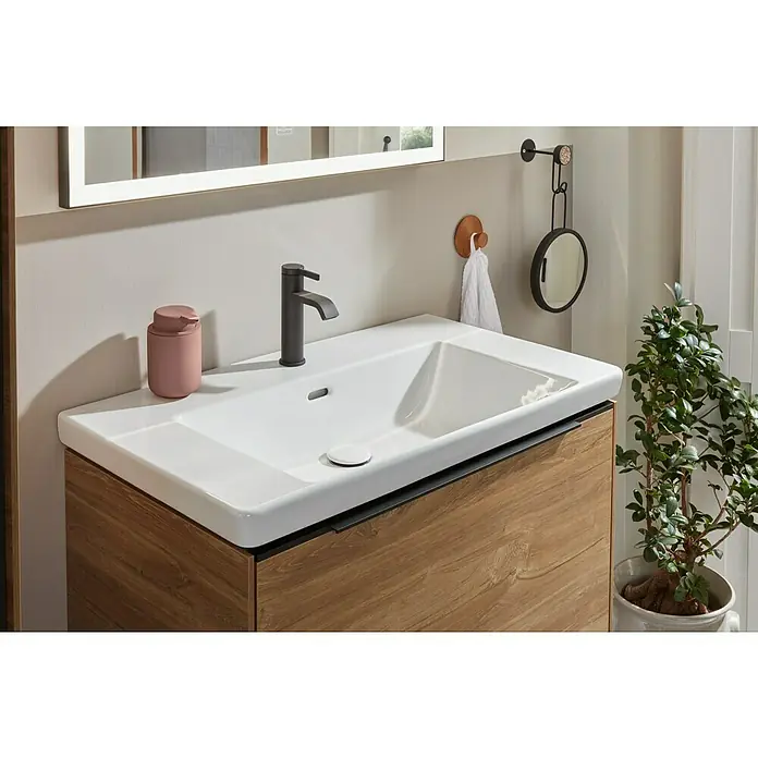 Villeroy & Boch Subway 3.0 Waschbeckenunterschrank - Kansas Oak, Anzahl Schubladen: 1 Stk., Farbe Griff: Volcano Black, B x T x H: 77,2 x 47,8 x 42,9 cm - Moderner Waschtisch mit weißem Keramikwaschbecken, dunkelgrauem Wasserhahn, hellem Holzschrank, pinkfarbenem Seifenspender und Spiegel.