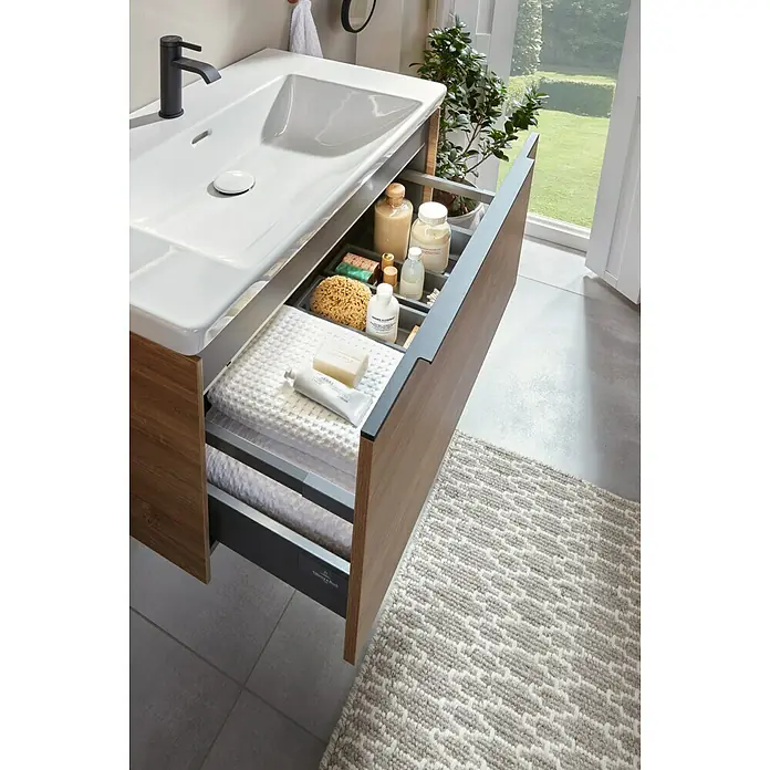Villeroy & Boch Subway 3.0 Waschbeckenunterschrank - Kansas Oak, Anzahl Schubladen: 1 Stk., Farbe Griff: Volcano Black, B x T x H: 77,2 x 47,8 x 42,9 cm - Moderner Badezimmer-Waschtisch mit weißem Waschbecken und schwarzem Wasserhahn. Offene Holzschubladen zeigen ordentlich arrangierte Toilettenartikel und weiße Handtücher.