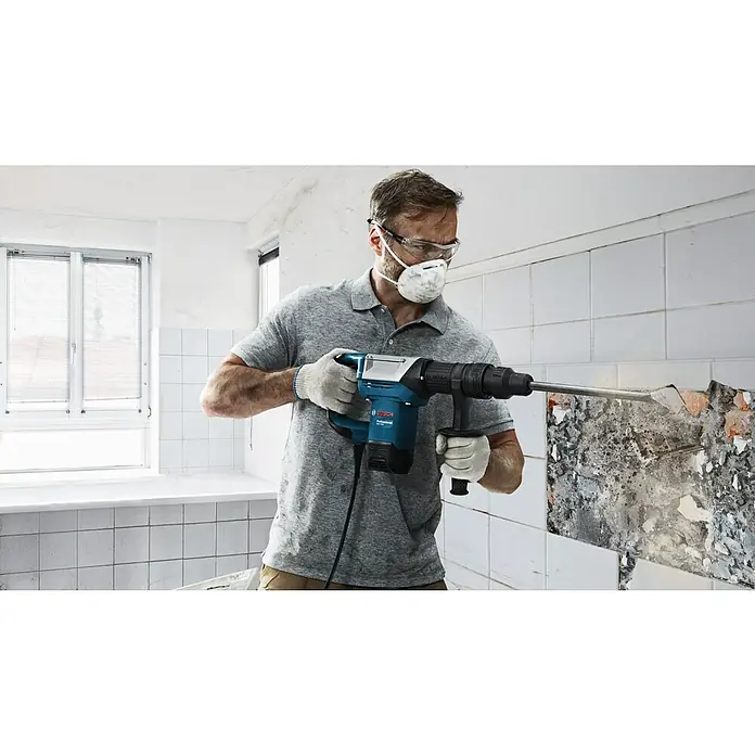 Bosch Professional Abbruchhammer GSH 5 - 1.100 W, 7,5 J, SDS-Max-Aufnahme - Bauarbeiter mit Schutzbrille und Maske benutzt einen Bosch Abbruchhammer, um Fliesen von einer Wand zu entfernen.