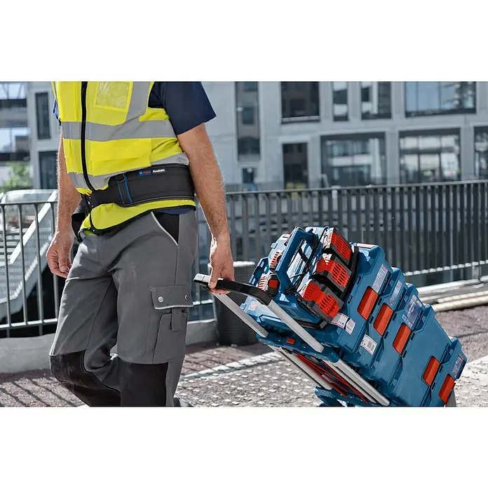 Bosch Professional AMPShare 18V Batterie-Ladegerät GAL 18V6-80 - Passend für: Bosch Professional 18 V Akku - Ein Bauarbeiter zieht einen blauen Bosch Werkzeugkofferwagen mit mehreren roten Batterien vor einem modernen Gebäude.