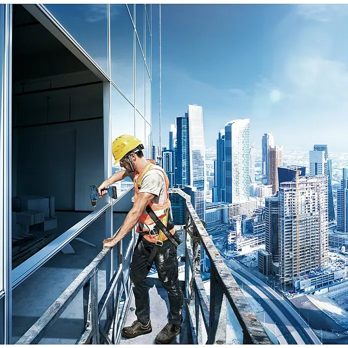 Bosch Professional AMPShare 18V Akku-Bohrschrauber GSR 18V-21 - 18 V, Ohne Akku, Ohne Koffer - Bauarbeiter mit gelbem Helm und Sicherheitsgurt montiert Fenster in einem Hochhaus mit einem Akkuschrauber.