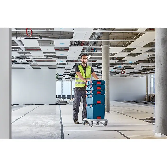 Bosch Professional Systemkoffer L-Boxx 238 - L x B x H: 357 x 442 x 253 mm, ABS - Ein Bauarbeiter schiebt einen Wagen mit gestapelten Werkzeugkoffern. Die robusten Koffer sind ideal für Baustellen und den Transport von Werkzeug.