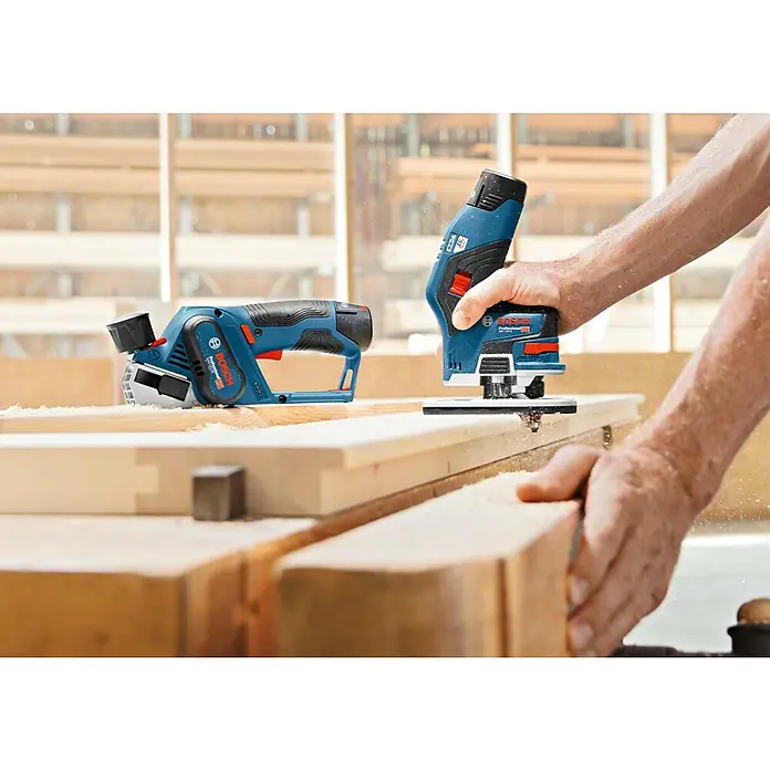 Bosch Professional Akku-Kantenfräser GKF 12V-8 - 12 V, Ohne Akku, Leerlaufdrehzahl: 13.000 U/min - Zwei Bosch-Elektrowerkzeuge: ein Hobel und eine Oberfräse, in Aktion auf Holz, ideal für präzise Holzbearbeitung.