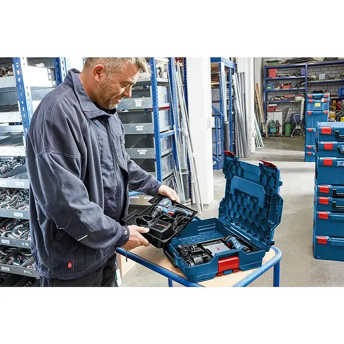Bosch Professional Systemkoffer L-Boxx 102 - L x B x H: 444 x 360 x 117 mm, ABS - Mann hantiert mit einem blauen Bosch Werkzeugkoffer, gefüllt mit Akkuschrauber und Zubehör, in einer Werkstatt.