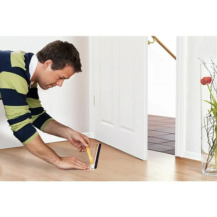 Tesa INSULATION Burlete para puerta Standard - 1 m x 12 mm, Puertas, Marrón - Un hombre aplica un sello de puerta para evitar corrientes de aire. El producto es fácil de instalar y proporciona un buen aislamiento.