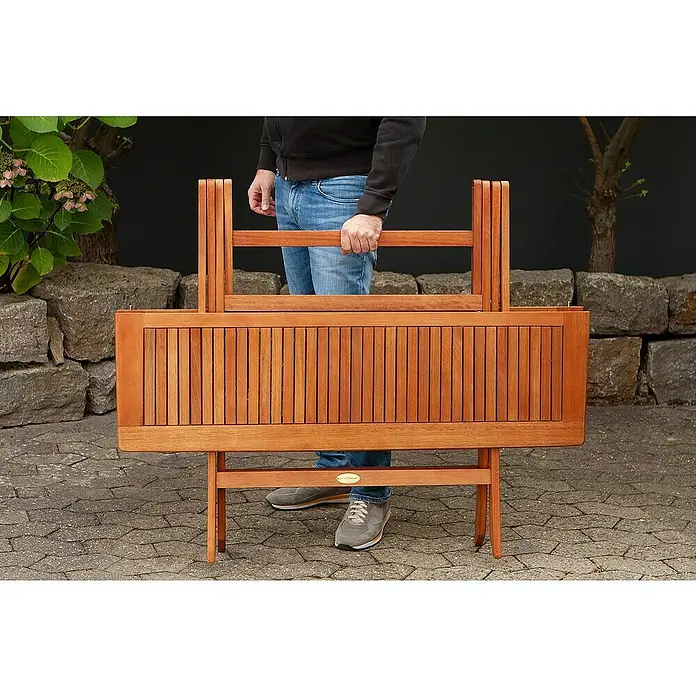 Garden Pleasure Gartentisch Orlando - L x B x H: 120 x 70 x 74 cm, Eukalyptus, Natur, Klappbar - Eine Person hält eine klappbare Gartenbank aus Holz, die ihr kompaktes Design und ihre Tragbarkeit zeigt.
