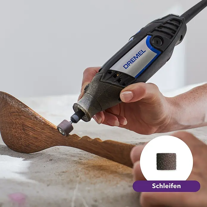 Dremel Multifunktionswerkzeug 3200 (1/90) - 130 W - Detailaufnahme eines Dremel-Rotationswerkzeugs beim Schleifen eines Holzobjekts, wobei ein Schleifeinsatz im Vordergrund hervorgehoben wird.