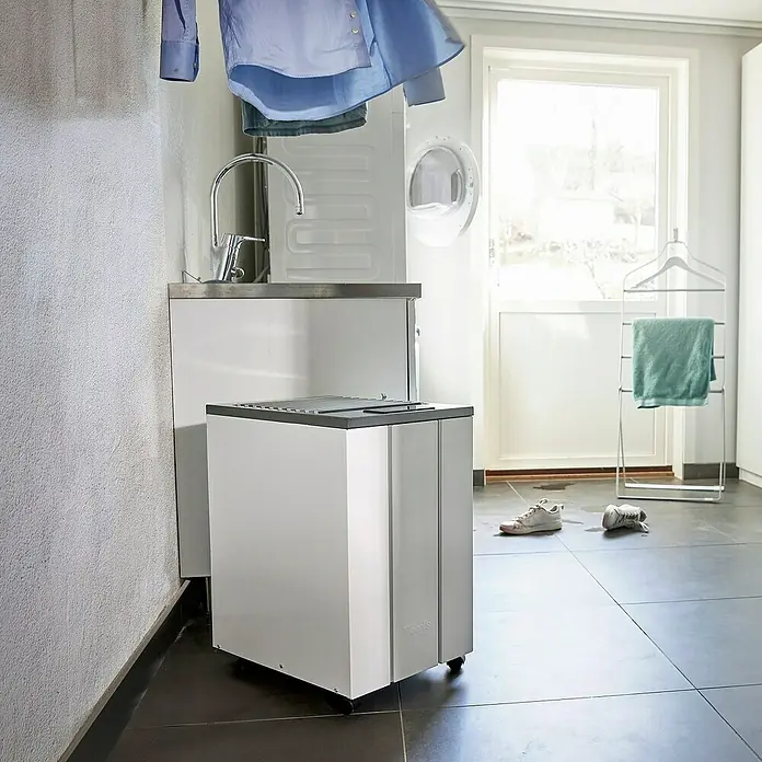 Woods Elektro-Luftentfeuchter LD 40 - 250 W, Entfeuchtungsleistung: 13 l/Tag, Weiß - Weißer Luftentfeuchter mit grauen Akzenten und Rollen, in einer Waschküche neben einem Waschbecken.