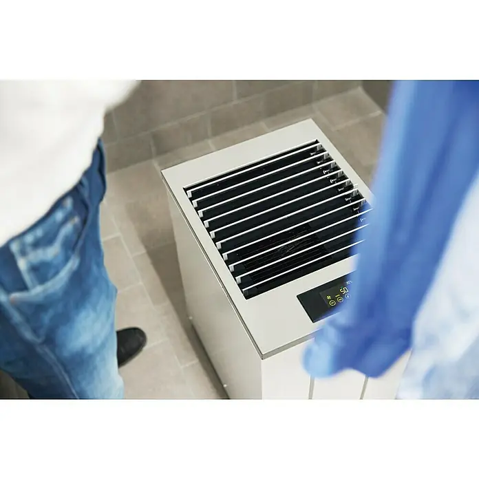 Woods Elektro-Luftentfeuchter LD 40 - 250 W, Entfeuchtungsleistung: 13 l/Tag, Weiß - Silbernes, bodenstehendes Klimagerät mit Lüftungsschlitzen und Digitalanzeige (20°C) neben einer Person.