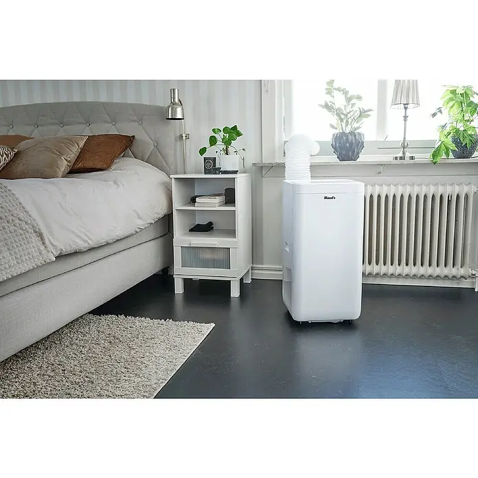 Woods Mobiles Klimagerät Milan 9K WIFI DUO - 2,6 kW, Raumgröße: 26 m², Weiß - Weißes, mobiles Klimagerät mit Abluftschlauch, das ein Schlafzimmer am Fenster kühlt.