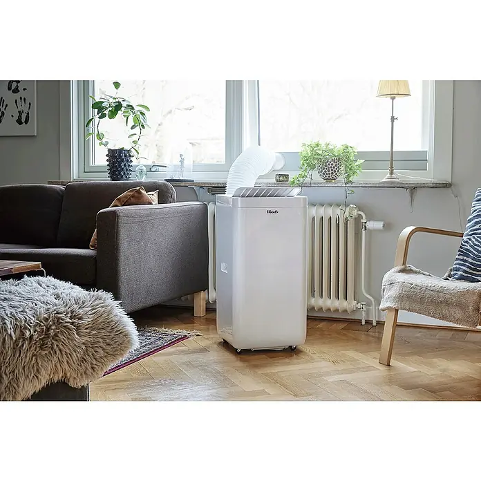 Woods Mobiles Klimagerät Milan 9K WIFI DUO - 2,6 kW, Raumgröße: 26 m², Weiß - Weißes, mobiles Klimagerät mit Abluftschlauch, der zu einem Fenster in einem Wohnzimmer führt.