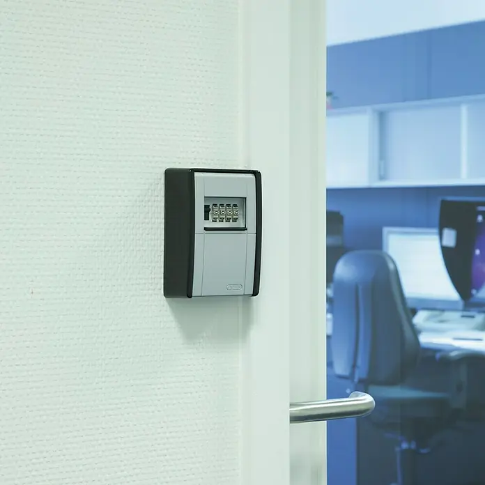 Abus Schlüsselbox Key Garage 787 - Geeignet für: Bis zu 20 Schlüssel, L x B x H: 45 x 80 x 120 mm, Ohne LED-Beleuchtung - Ein Schlüsseltresor mit Zahlenschloss ist an einer weißen Wand neben einer geöffneten Tür montiert, ideal für die sichere Schlüsselaufbewahrung.