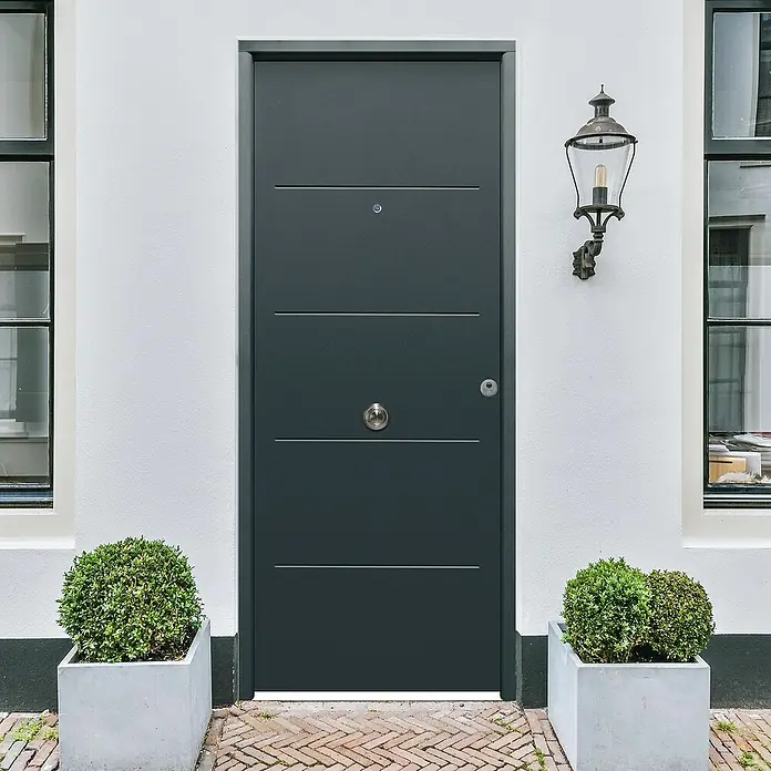 THT Puerta de entrada exterior Saga 100 - Izquierda, 90 x 210 cm, Antracita - Diseño moderno de puerta de entrada gris con líneas horizontales, enmarcada por paredes blancas y plantas verdes, creando una zona de entrada acogedora.