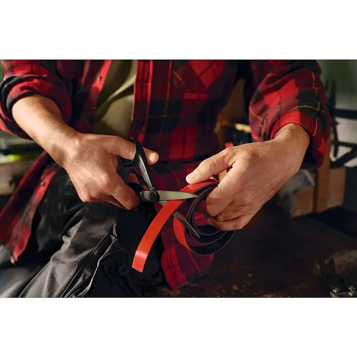 Tesa Ultra Power Klettpad Lock Tape - L x B: 1 m x 25 mm, Schwarz - Jemand schneidet ein Klettband mit einer Schere. Gut geeignet zum einfachen Organisieren und Befestigen von Objekten im Haushalt.