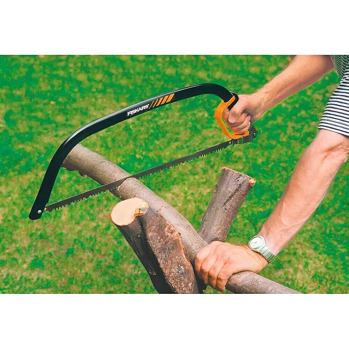 Fiskars Bügelsäge SW30 - L x H: 625 x 19 mm - Nahaufnahme einer Handsäge von Fiskars beim Sägen eines Holzstücks, wobei die schwarze Rahmenkonstruktion und der orangefarbene Griff deutlich zu sehen sind.