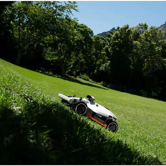 Mammotion Mähroboter Luba 2 AWD 3000X - 3.000 m², Schnittbreite: 400 mm, Satellitengestützte Navigation, GPS - Weißer und oranger Mähroboter mit schwarzen Rädern, der Gras an einem grünen Hang mäht.