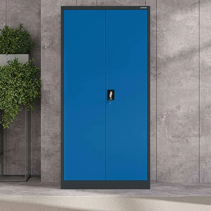 Jan Nowak Aktenschrank Jan - B x T x H: 90 x 40 x 185 cm, Anthrazit/Blau - Blauer Metall-Doppeltürschrank mit Schlüssel im Schloss, steht vor einer Betonwand neben einer großen Topfpflanze.