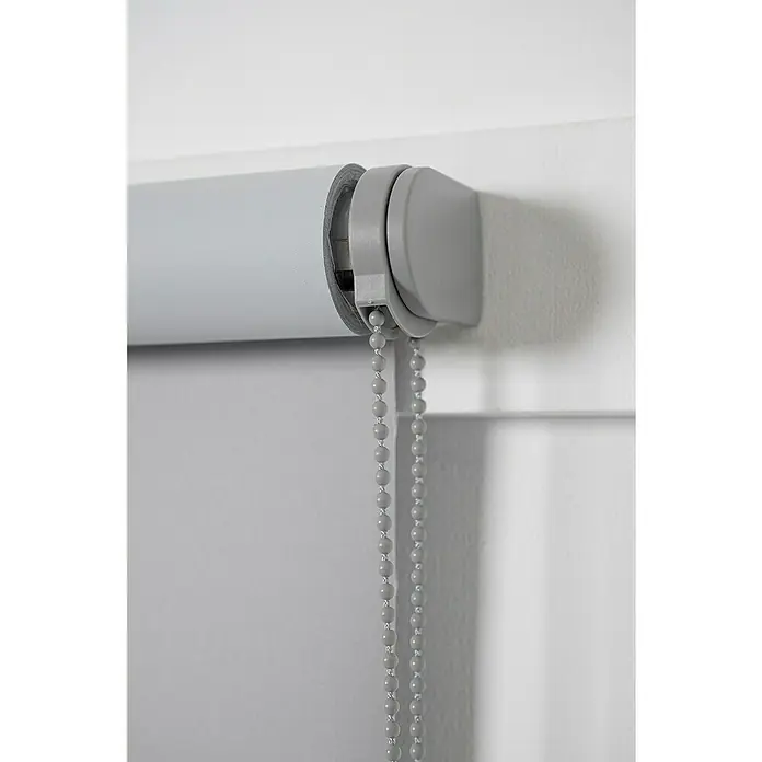 Estor enrollable opaco NDC - An x Al: 90 x 250 cm, Gris - Primer plano de una persiana enrollable gris con una cadena de bolas para su accionamiento, montada en una pared blanca.