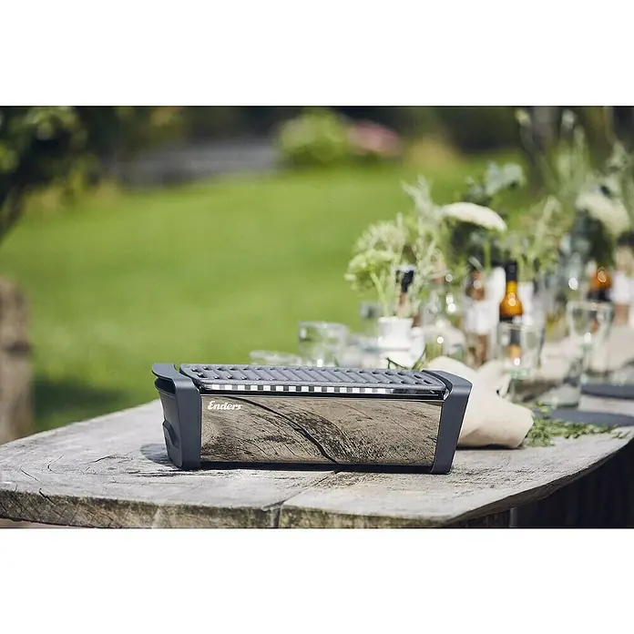 Enders Elektrogrill Aurora - MIrror-Schwarz, Grillfläche (B x T): 37 x 25 cm - Ein tragbarer Enders-Grill mit Edelstahlgehäuse und dunkelgrauem Rost steht auf einem Holztisch im Freien.