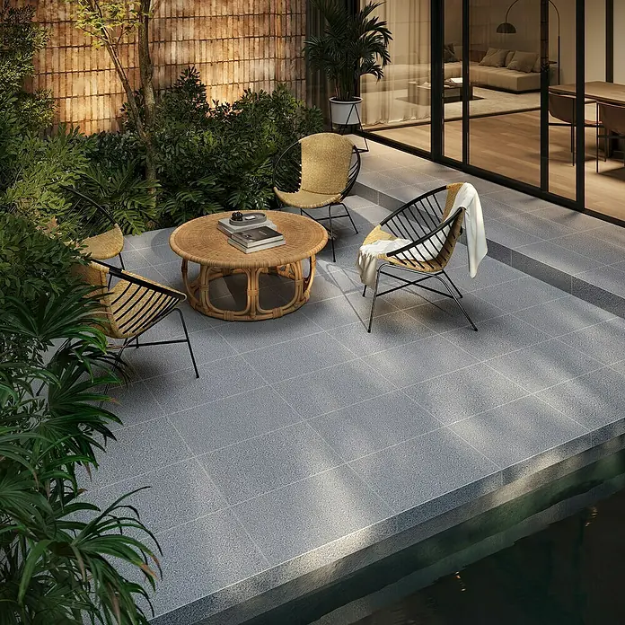 Terrassenplatte G654 - 60 x 60 x 3 cm, Anthrazit, Granit - Draufsicht auf eine stilvolle Terrassengarnitur mit Rattansesseln und Tisch auf einer grauen, gefliesten Terrasse neben einem Pool.