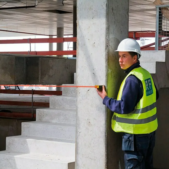 Stabila Laserentfernungsmesser LD 320 - Messbereich: 0,05 - 40 m - Ein Bauarbeiter in Arbeitskleidung misst mit einem Rollbandmaß einen Betonpfeiler auf einer Baustelle. Schutzhelm und Warnweste sind wichtige Bestandteile seiner Ausrüstung.