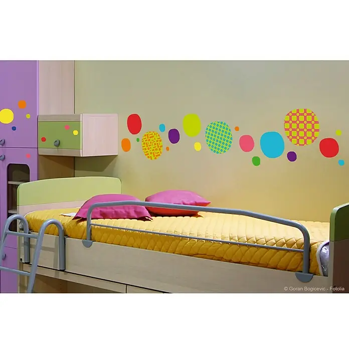 Vinilo de pared Burbujas colores - 48 x 68 cm, Multicolor, Plástico - Habitación infantil con una cama individual, colchón amarillo y patrones de puntos coloridos en la pared. Un espacio acogedor para un niño.