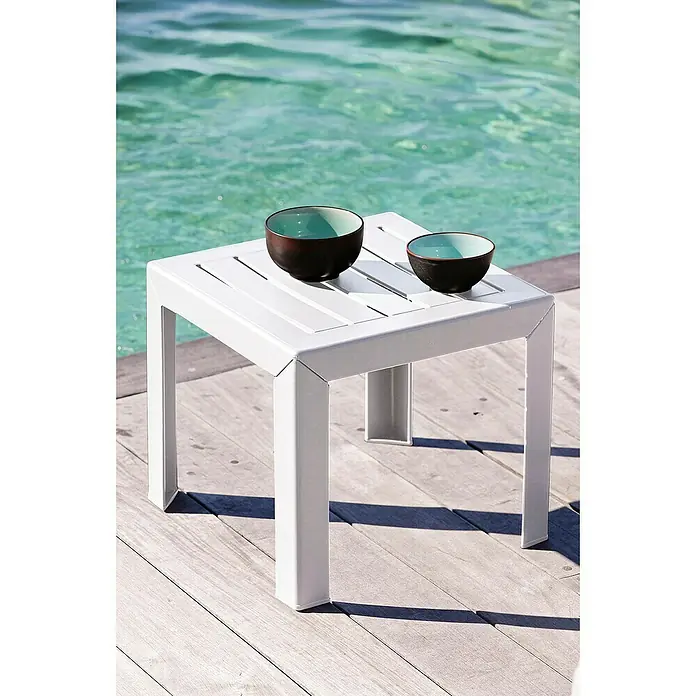 Grosfillex Garten-Beistelltisch Miami - L x B x H: 40 x 40 x 35 cm, Polypropylen, Stapelbar, Rechteckig, Weiß - Weißer quadratischer Beistelltisch mit Lattenplatte, zwei Schalen haltend, auf Holzdeck am Wasser.