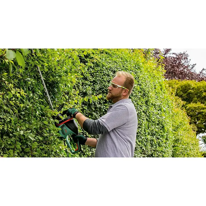 Bosch Power for All 36V Akku-Heckenschere AdvancedHedgeCut 36V-65-2836 V, Li-Ionen, Ohne Akku - Ein Mann trimmt eine Hecke mit einer grünen Bosch Heckenschere. Er trägt dabei eine Schutzbrille und Handschuhe.